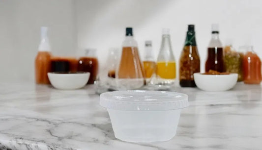 2oz PP clear portion pot (PP2) on a marble surface with blurred bottles and bowls in the background