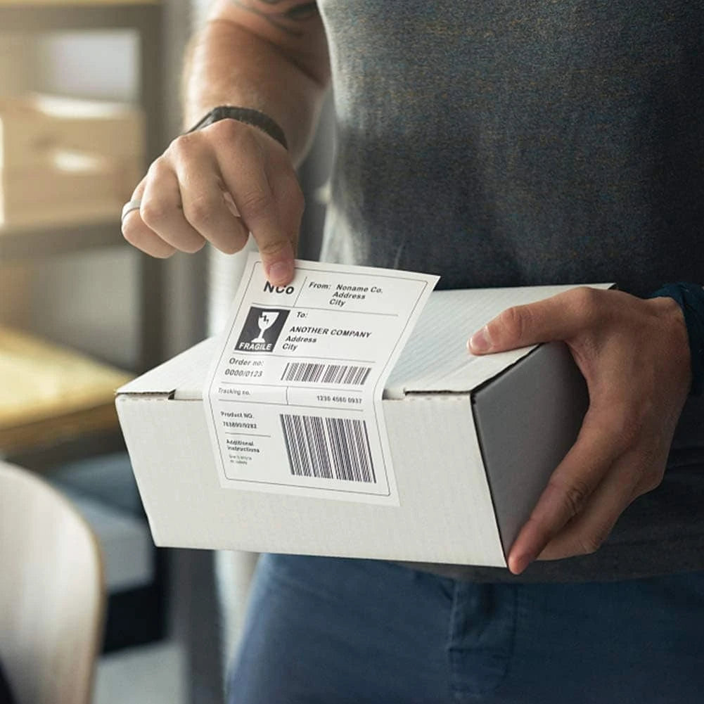 Person holding a package with a shipping label on a blurred indoor background