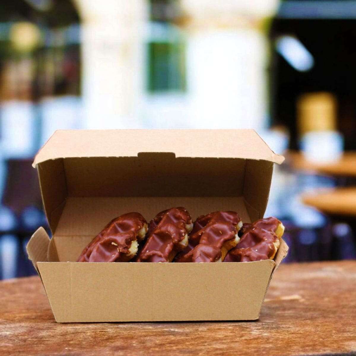 Corrugated clam shell box of chocolate-covered donuts on a wooden table with a blurred background