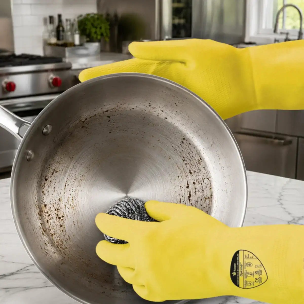 Durable Household Yellow Rubber Gloves being worn by a person inside a dirty stainless steel pan, scrubbing with a steel wire sponge on a marble countertop in a kitchen.