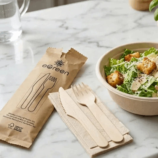 Biodegradable cutlery set with eGreen packaging on a marble surface next to a salad.