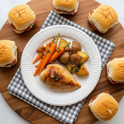6 White Greenspirit Paper Plated dish with chicken, carrots, and potatoes on a checkered cloth, surrounded by sandwiches on a wooden board.