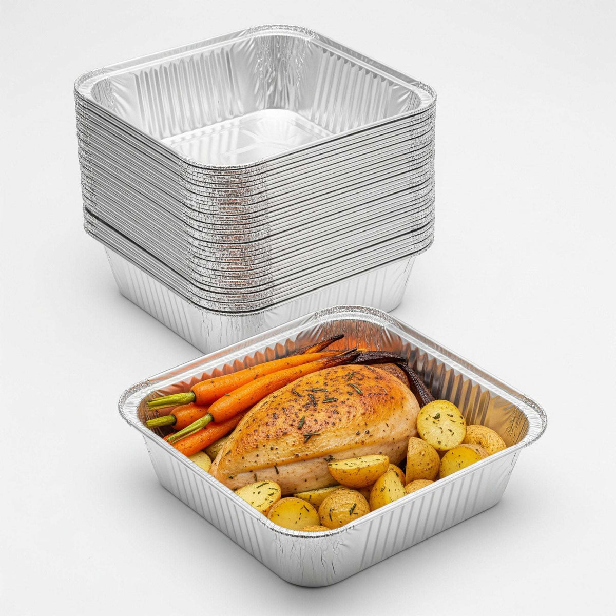 Stack of aluminum food containers with a partially filled one containing roasted vegetables and chicken.