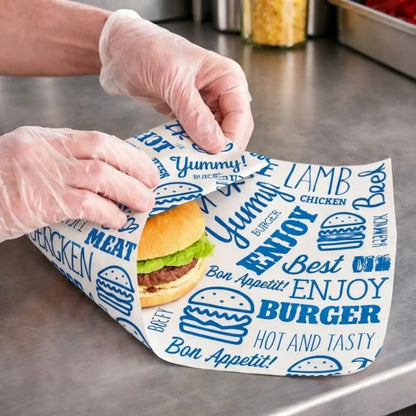 Person wearing gloves wraping a burger in Blue Compostable Burger Wrap on a metallic surface.