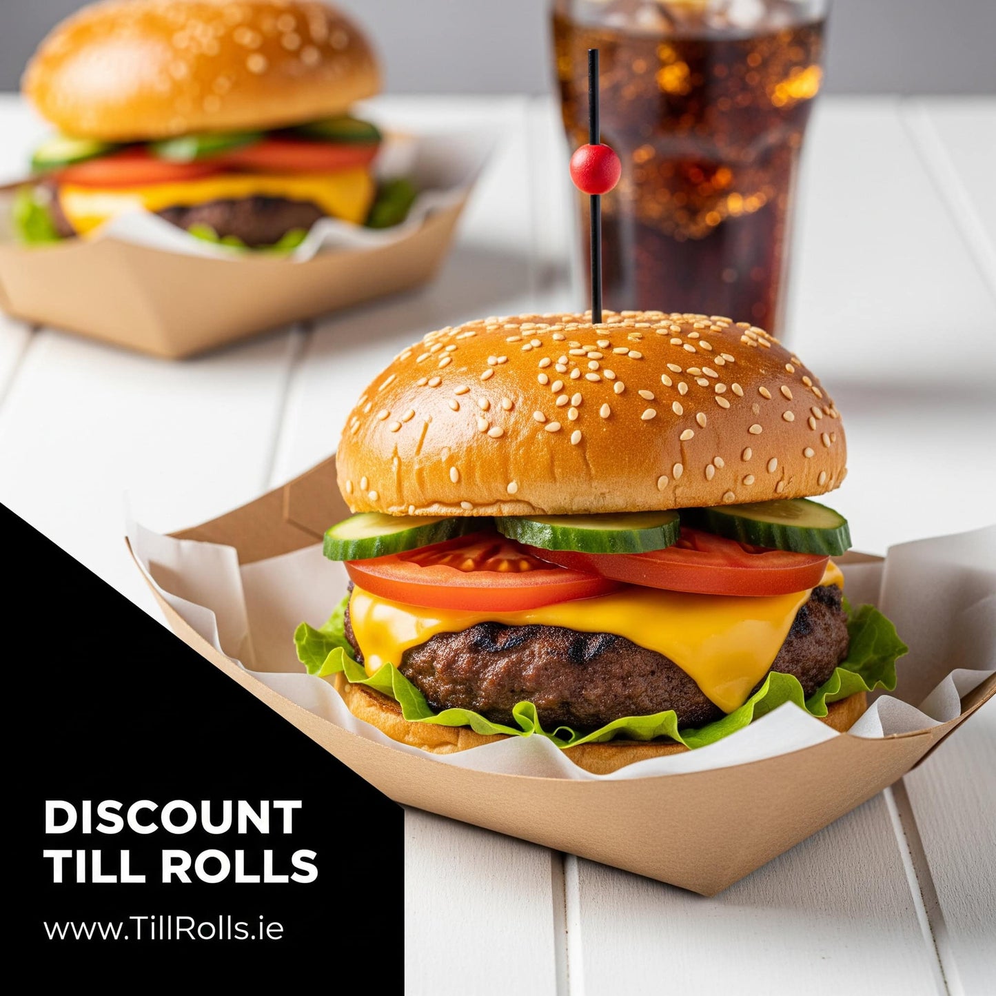 Hamburger with cheese, lettuce, tomato, and cucumber in a sesame seed bun, served in a 3lb Kraft Greenspirit Paper Food Trayr with a drink on a white wooden table.