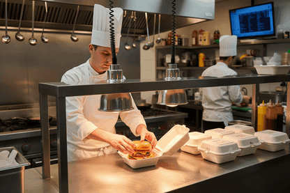 Chef preparing burgers in bagasse boxes under heat lamps