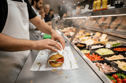 Deli staff member wrapping long bread roll in Greenspirit greaseproof sheets